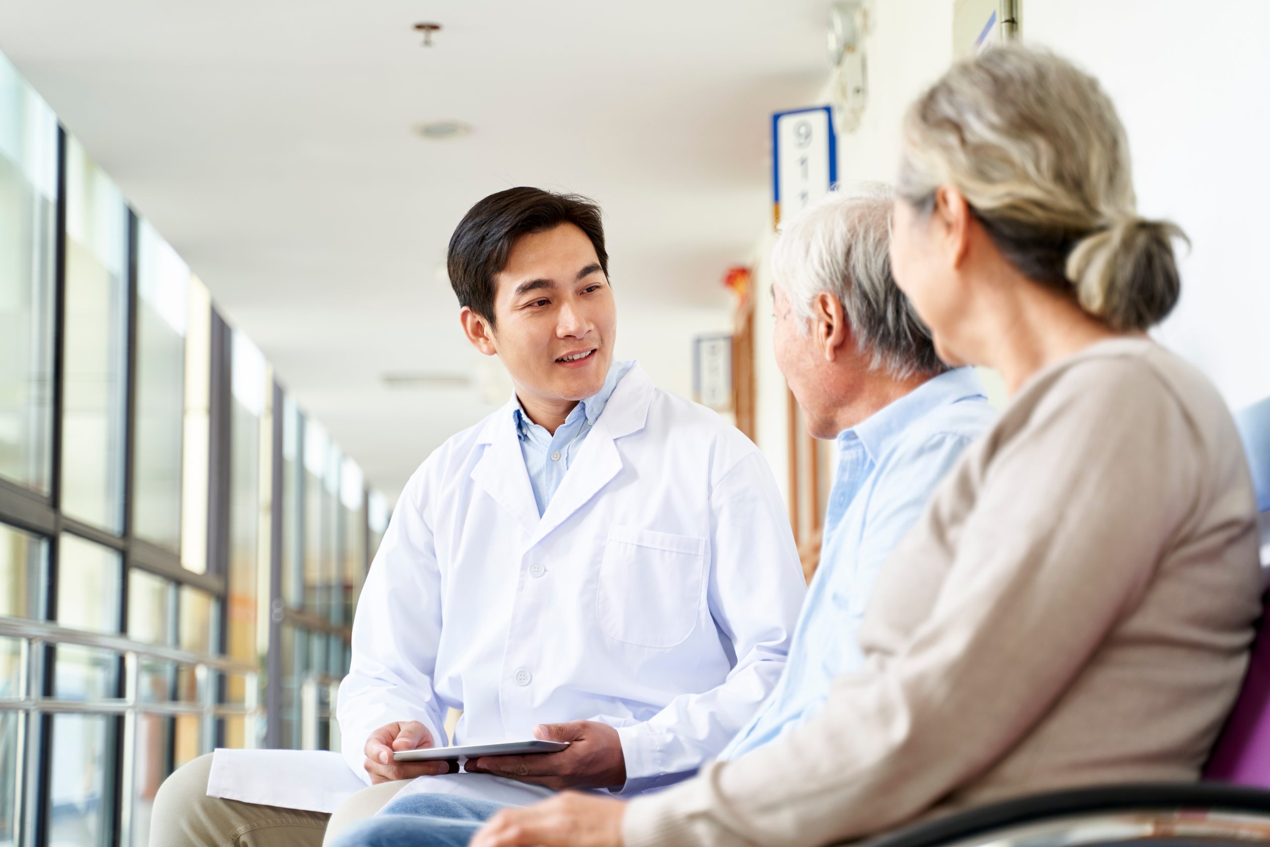 young asian doctor talking to senior couple patients in hospital hallway